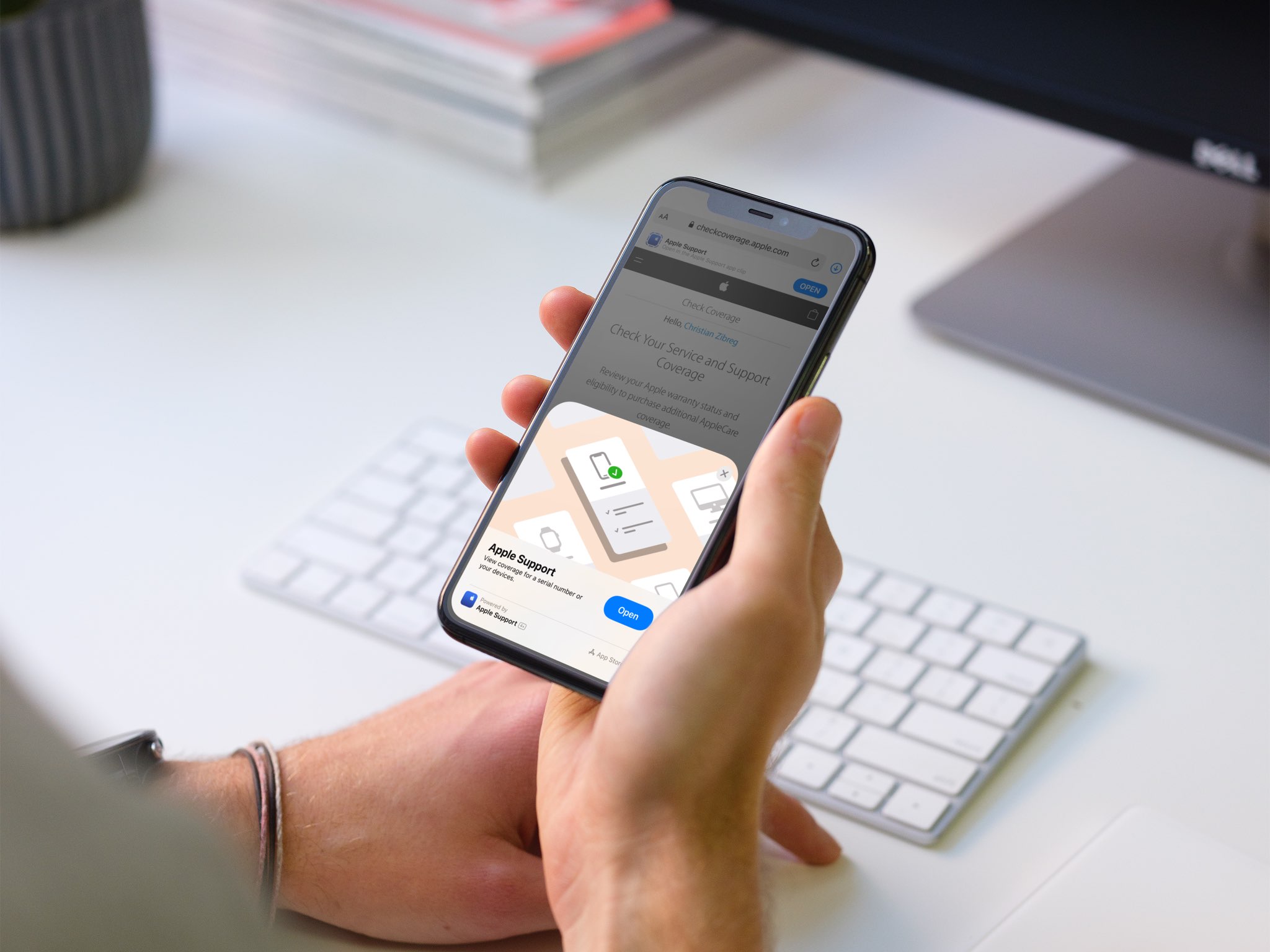 An image showing a person sitting at their desk, holding an iPhone in their hand with the Apple Support App Clip displayed on the screen