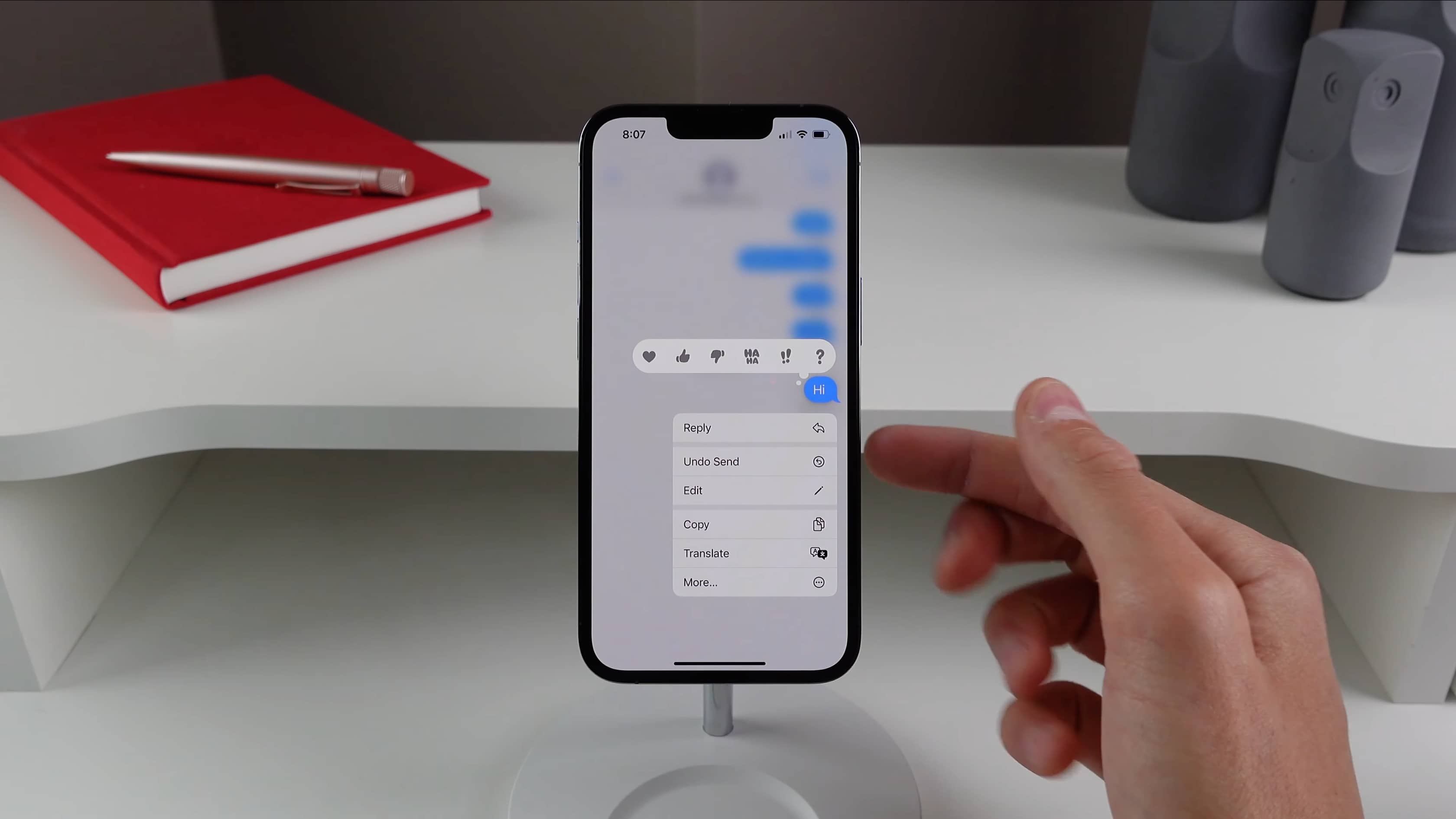 An iPhone on a stand running the Messages app, with the contextual menu displaying options include the new Undo Send feature in iOS 16