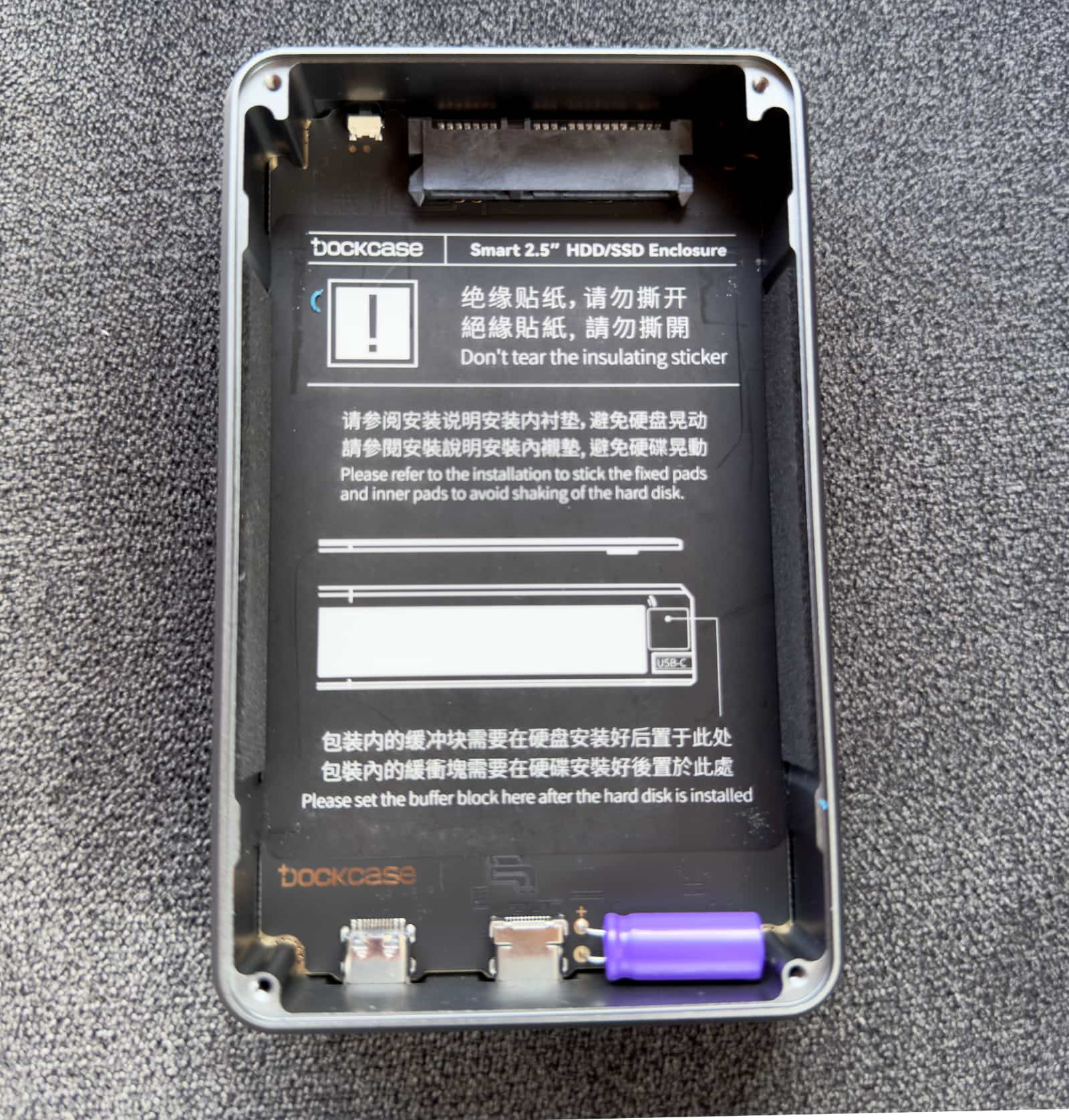 A top-down view of the DockCase external storage enclosure with the metal cover removed, exposing an insulating sticker, SATA III interface and capacitor on the inside