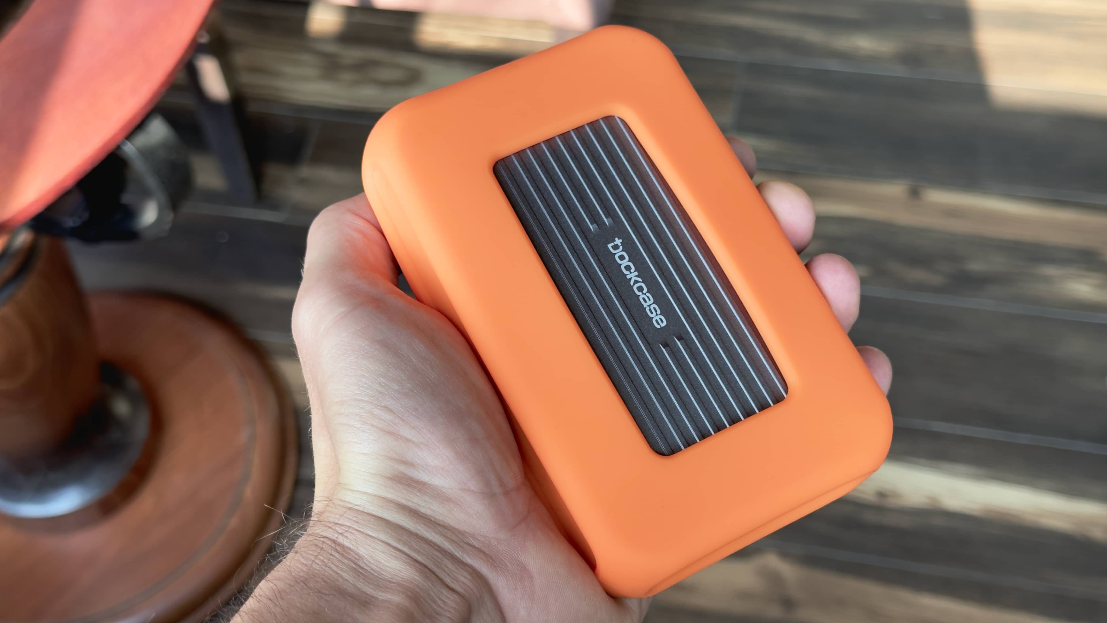Male hand holding a DockCase external storage enclosure in an orange protective case