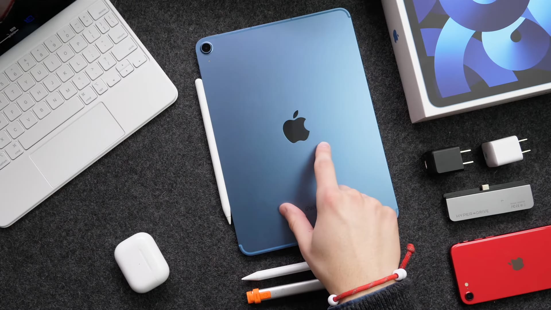 A top-down photograph showing a young male's right hand with the index finger pointing at a blue iPad Air 5 laid flat on a table facedown