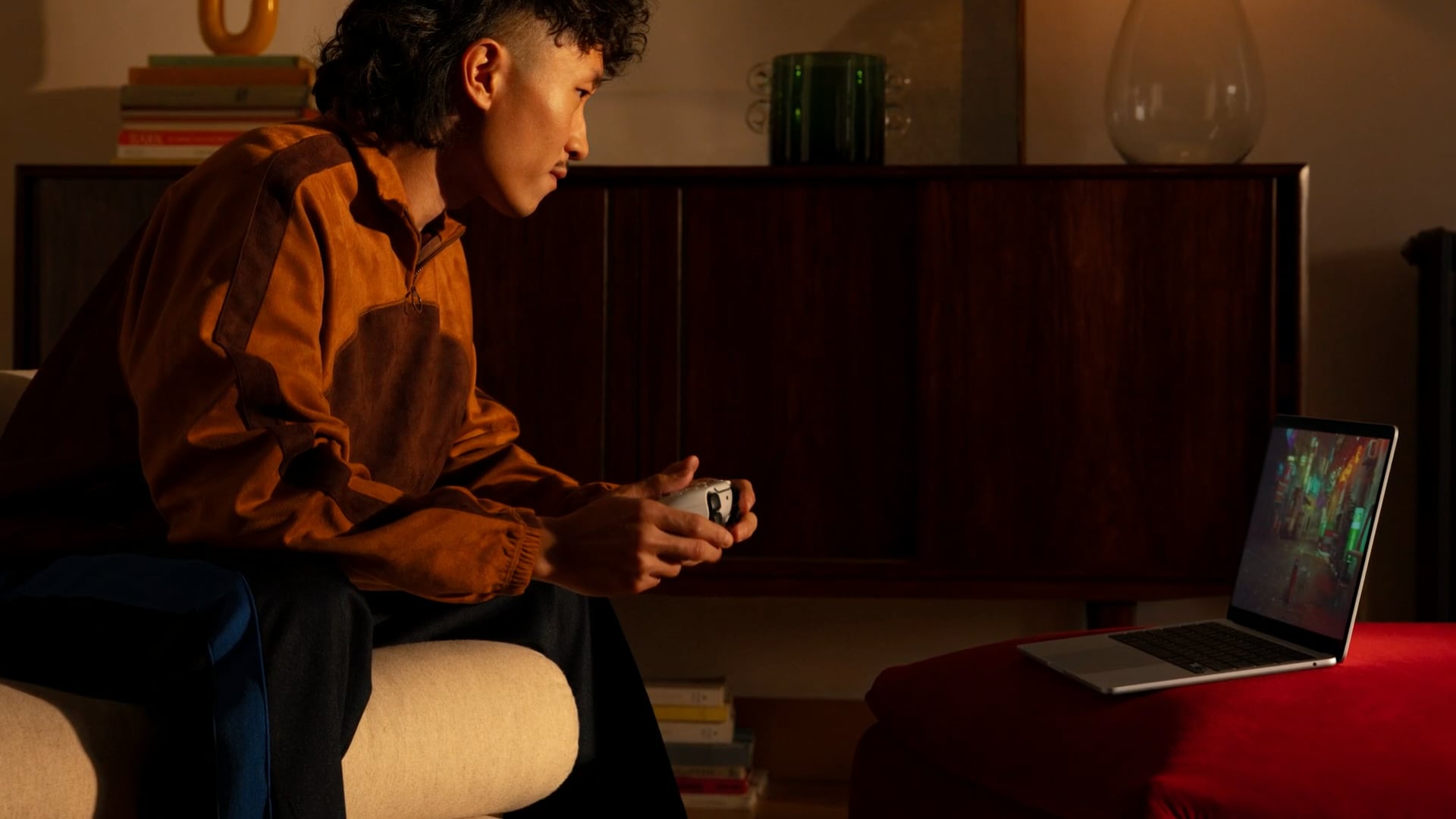 Lifestyle image depicting a young man playing a game on a MacBook Pro, using Sony's PS5 controller