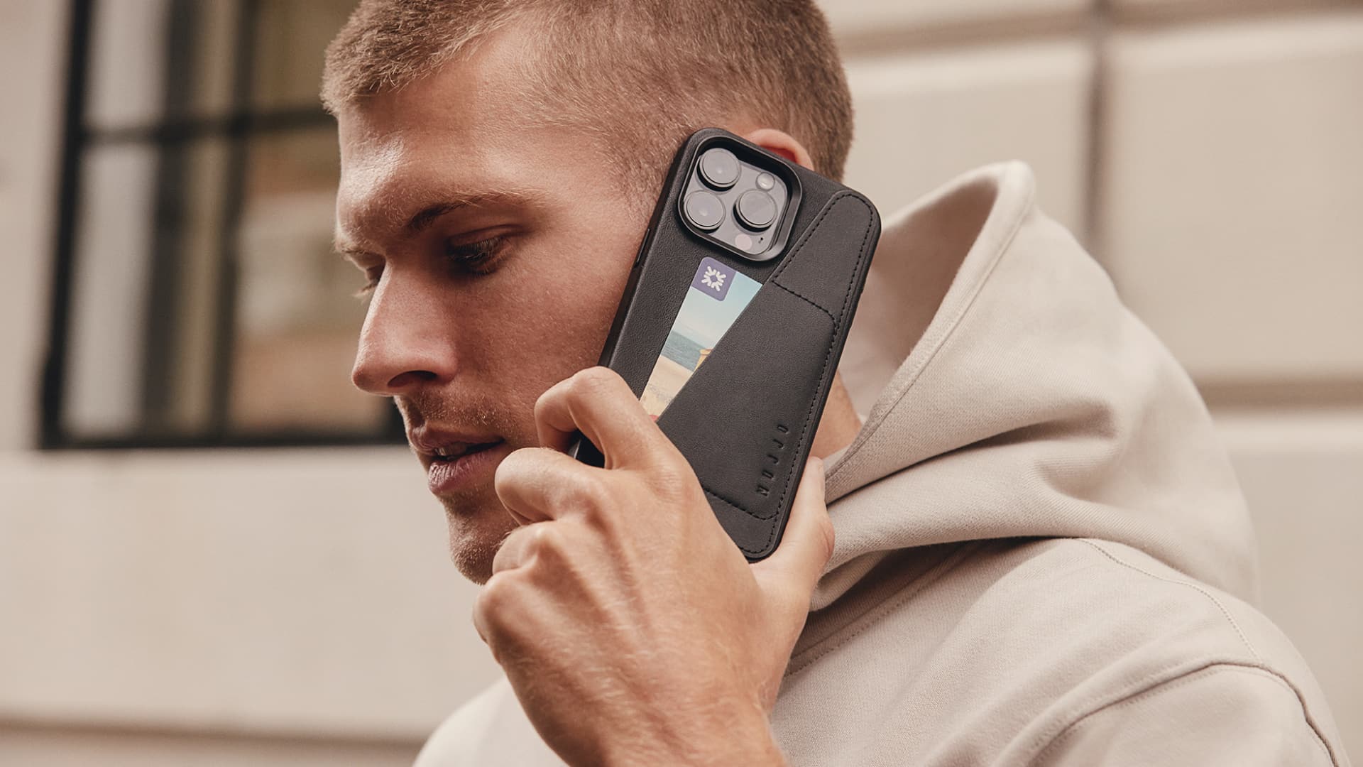 Guy holding iPhone 15 Pro Max in Mujjo's leather wallet case close to their ear