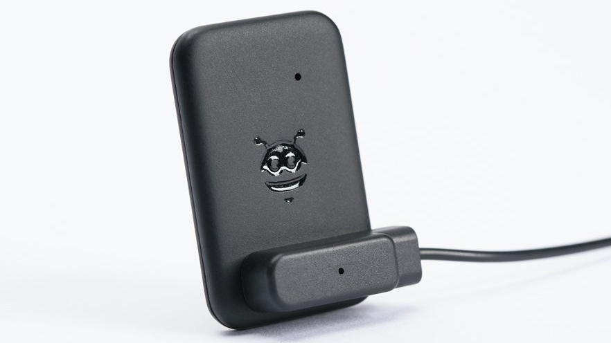 The rear side of a Pebblebee Tag tracker with a magnetic charge cable connected