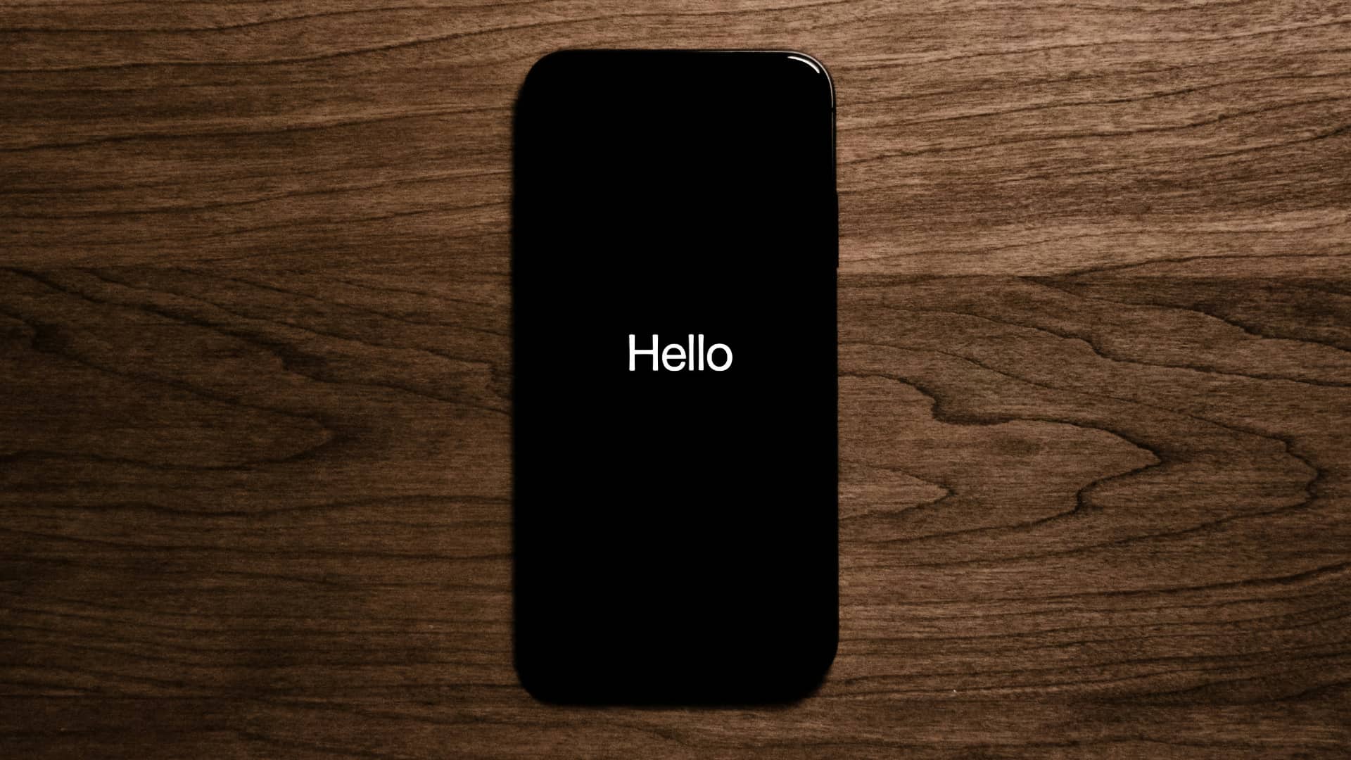 iPhone on wooden surface, displaying a Hello message on the screen