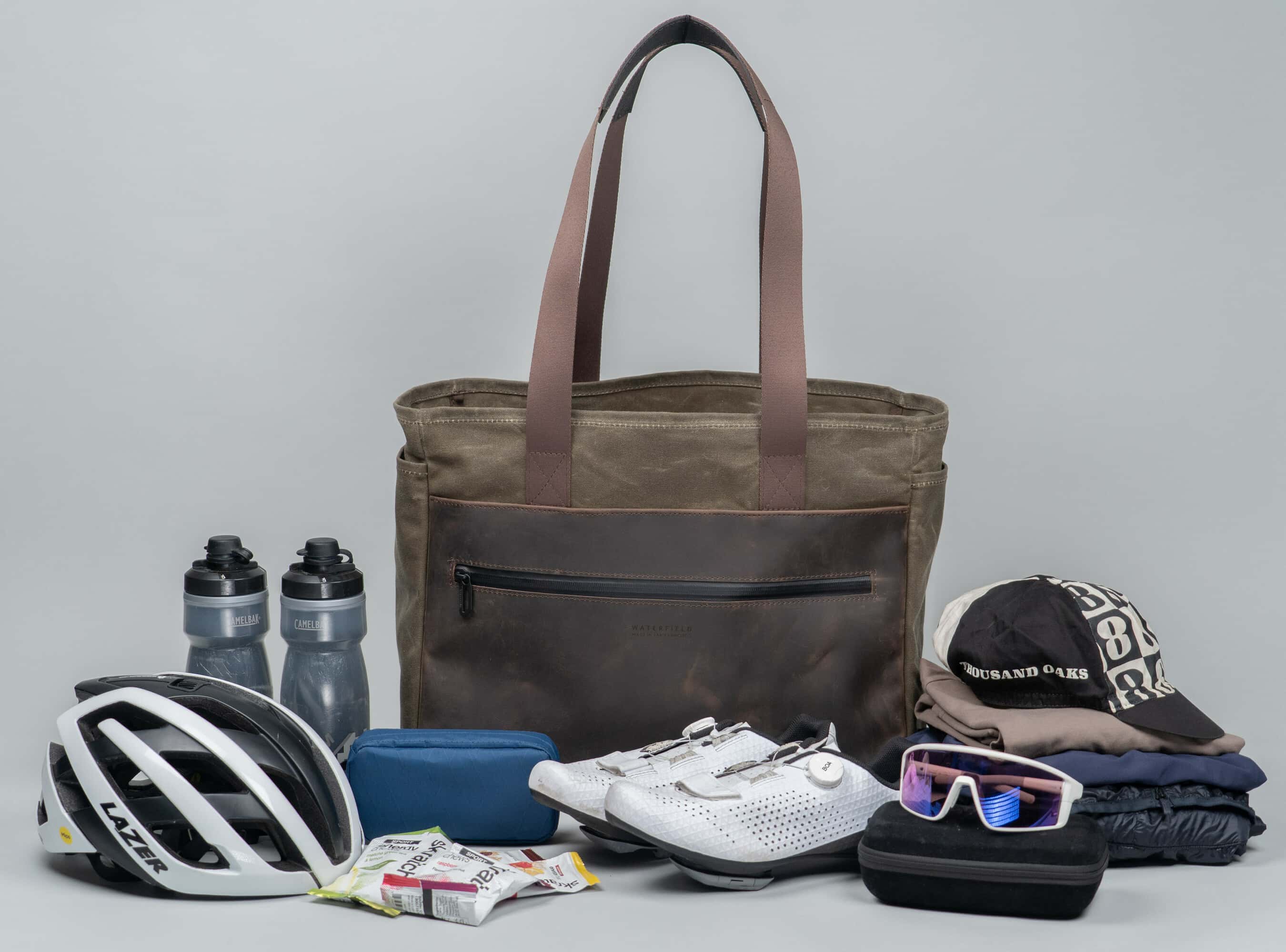 WaterField's leather cycling tote with a helmet, shows, sunglasses and other equipment in front of it