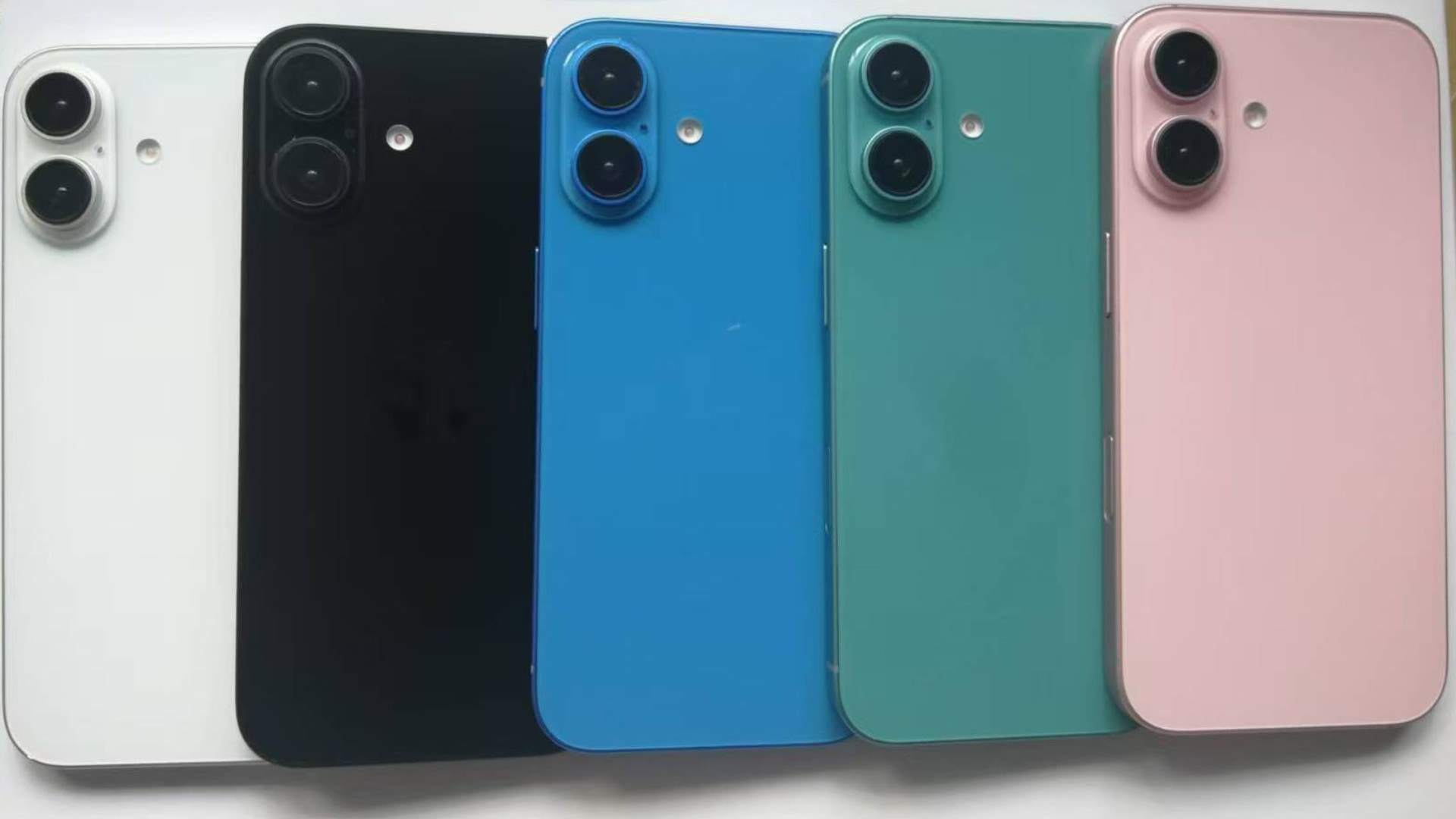 Four iPhone 16 dummy units facedown on white paper, showcasing new colors and vertical cameras.