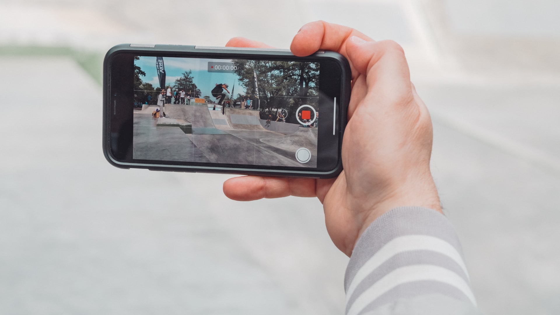 Closeup of a male hand holding an iPhone, recording skateboard stunts