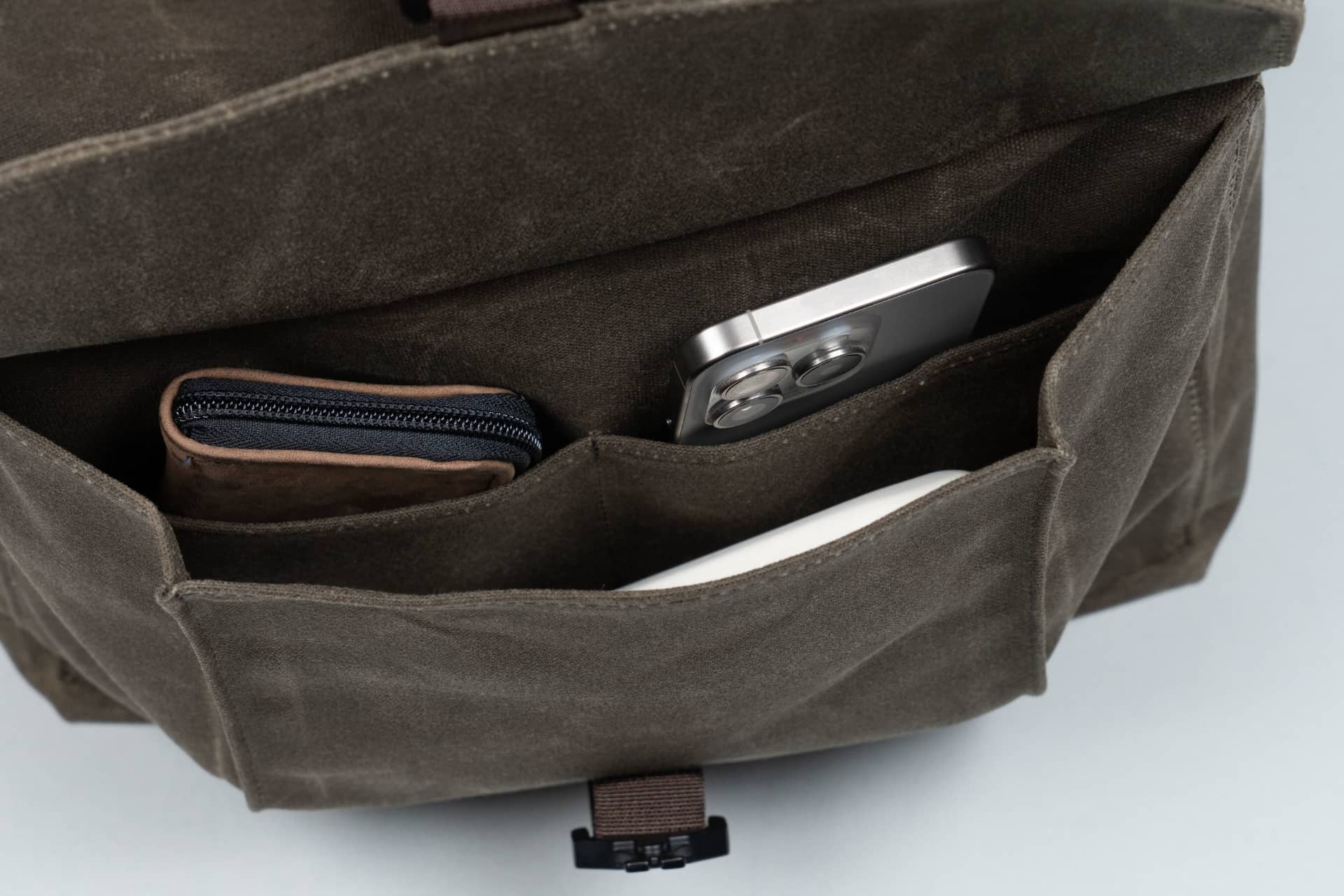 The front pocket of WaterField's Vitesse Backpack with an iPhone, AirPods and a wallet in the three interior pockets.