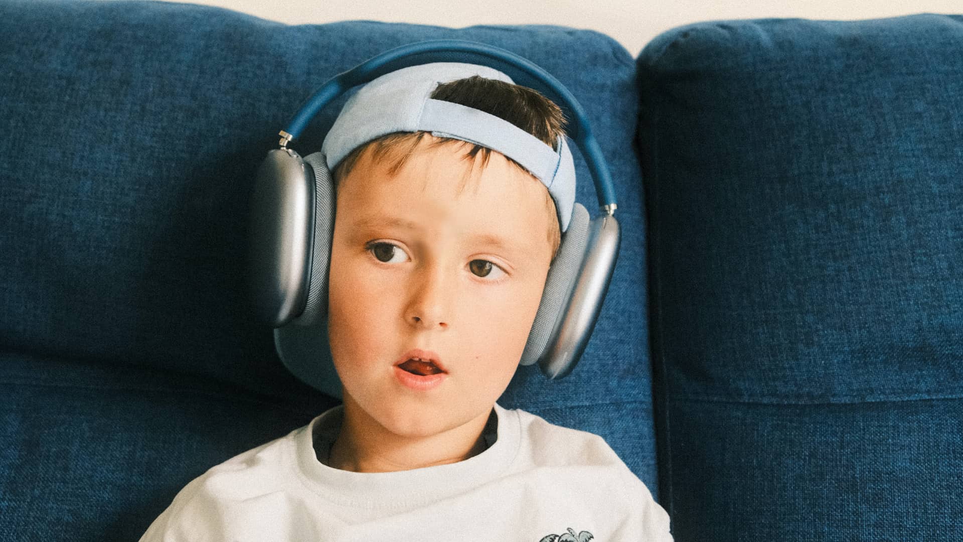 Little boy sitting on a couch, wearing AirPods Max headphones