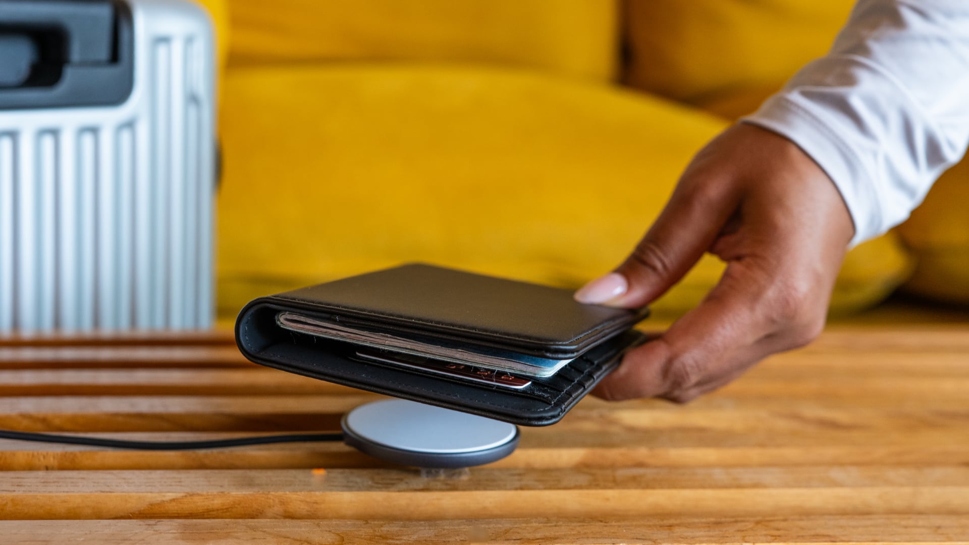 A female hand holding a Satechi passport cover above a wireless charger on a wooden desk.