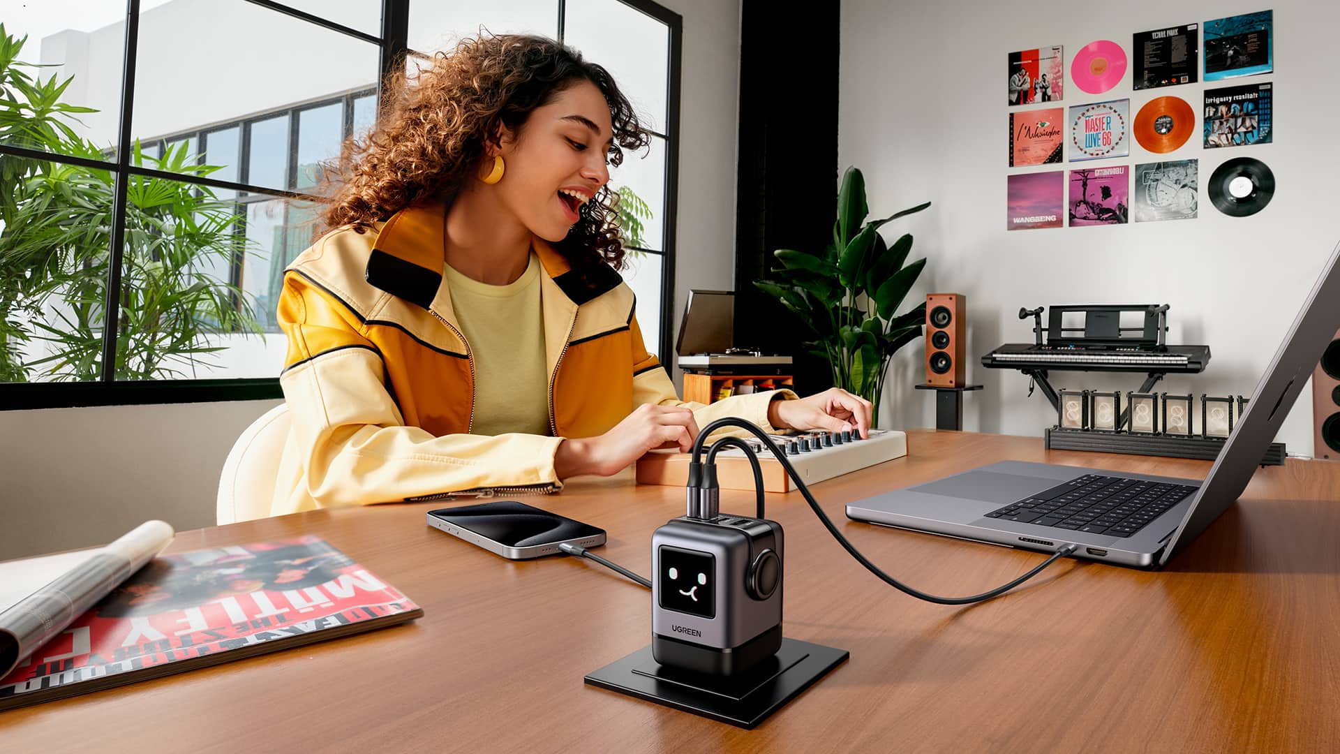 Woman sitting at a wooden desk in a stylish studio apartment, with her iPhone and MacBook Pro plugged into a Ugreen Uno charger.