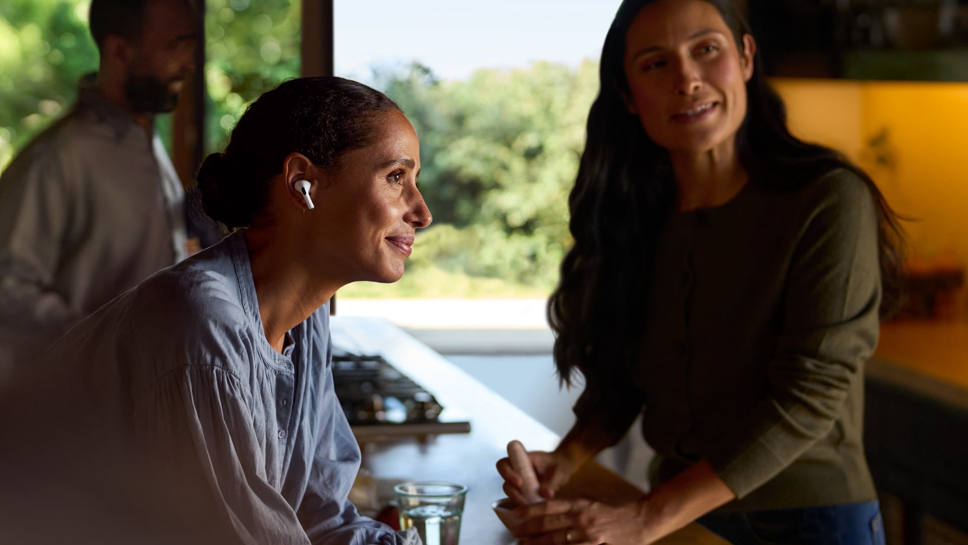 Two women and a guy gathered around a table, with one person wearing AirPods Pro 2.