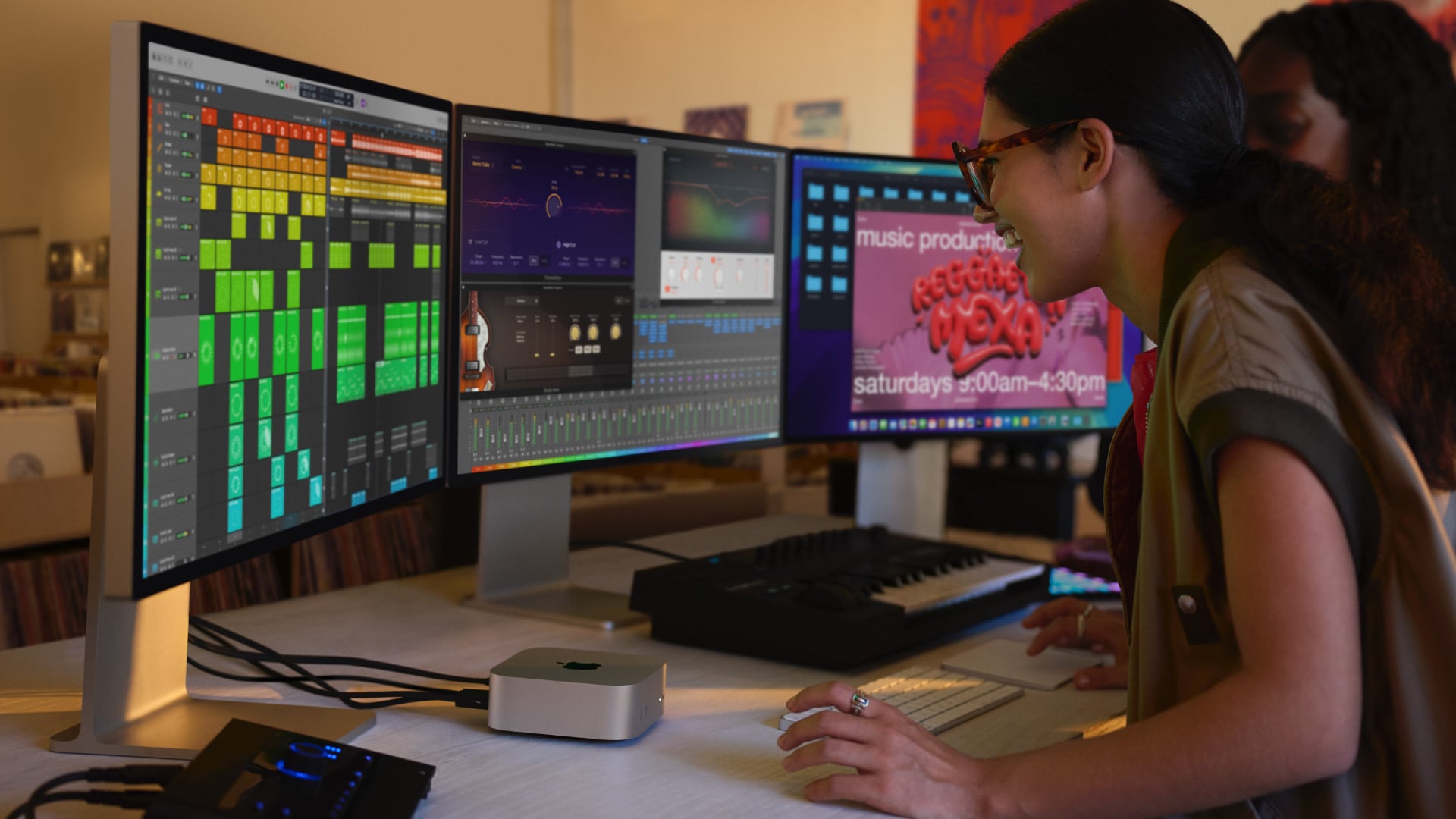 Two young woman sitting in a home music studio, sitting in front of three monitors connected to a Mac mini.