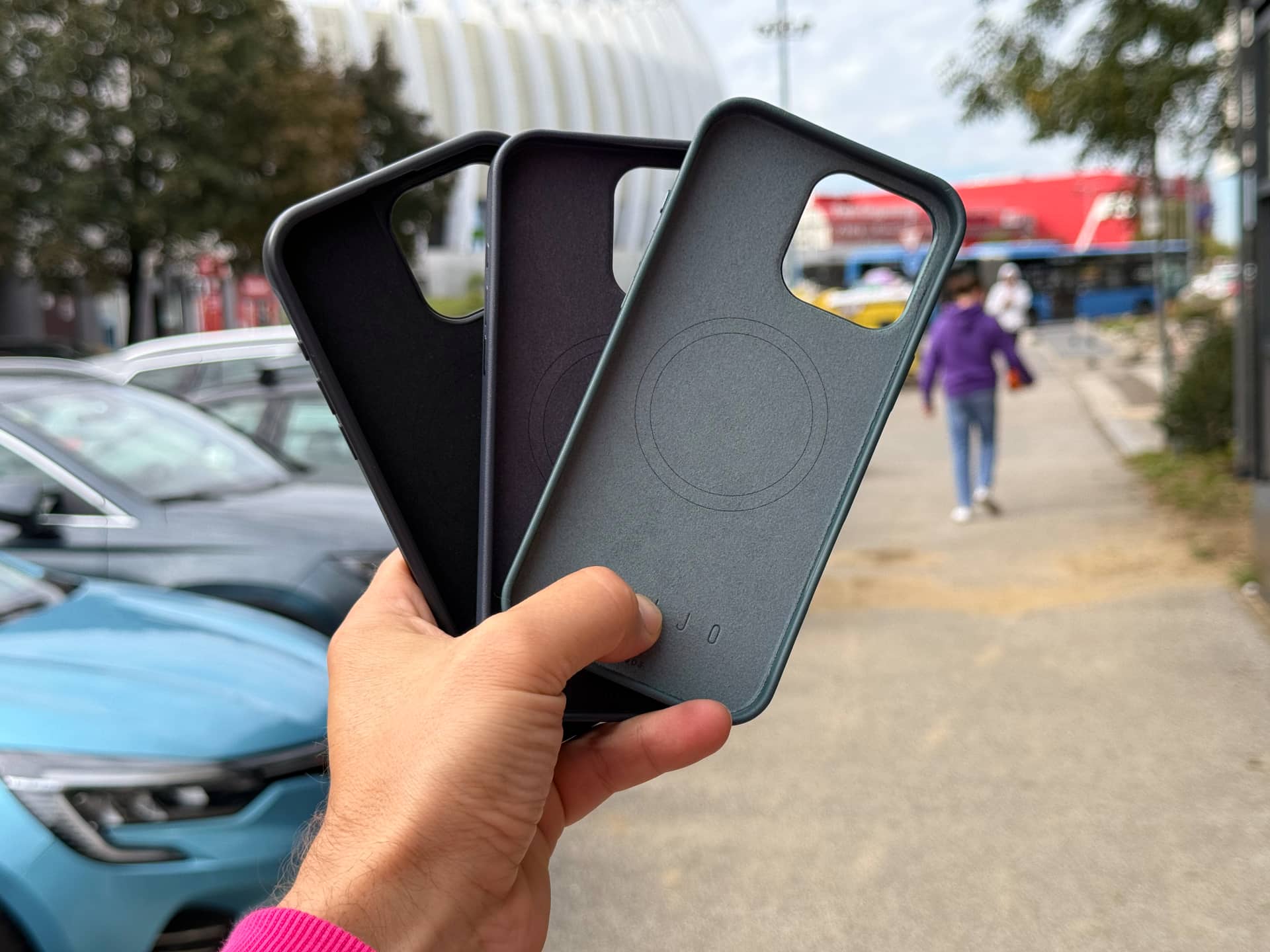 Hand holding three fanned out Mujjo iPhone 16 cases.