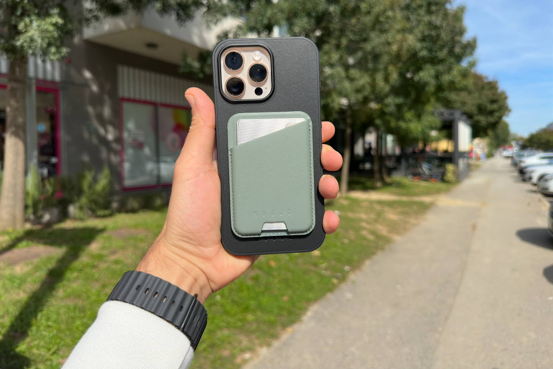 Hand holding Mujjo's Shield Case for iPhone 16 Pro Max with MagSafe wallet.