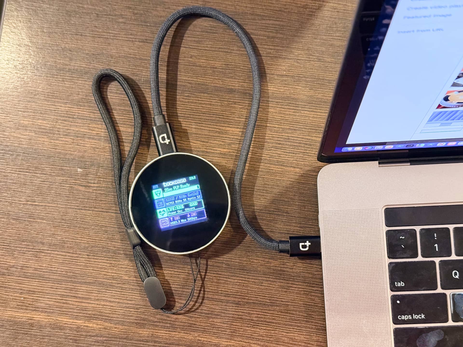 Closeup of a Dockcase MagSafe SSD enclosure on a wooden desk, plugged into a Mac laptop.