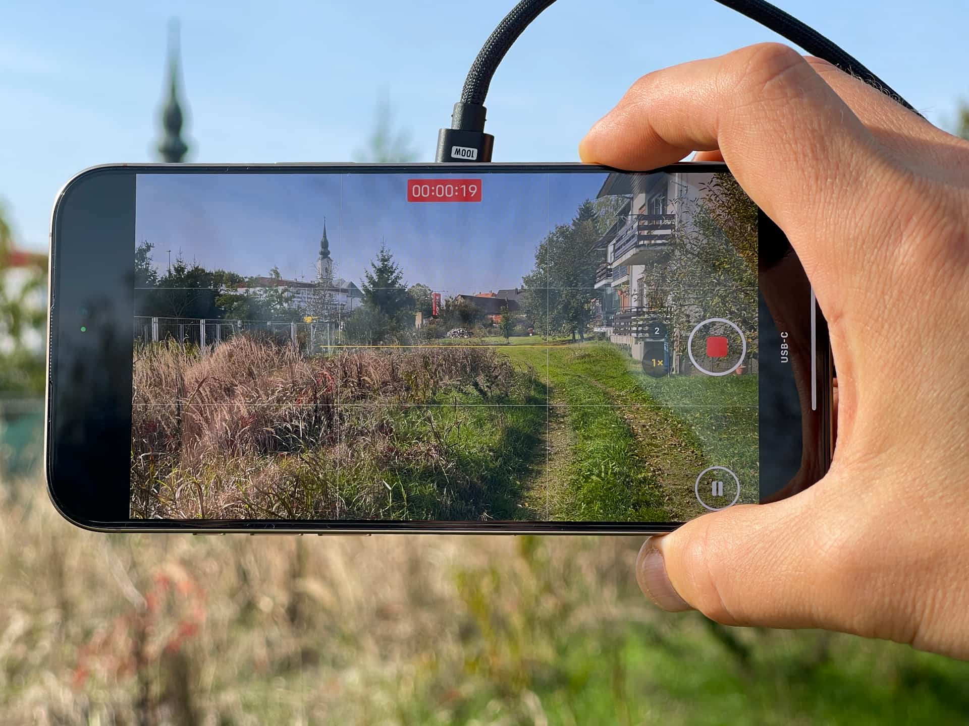 Male hand holding an iPhone in landscape orientation , shooting a ProRes video outdoors.