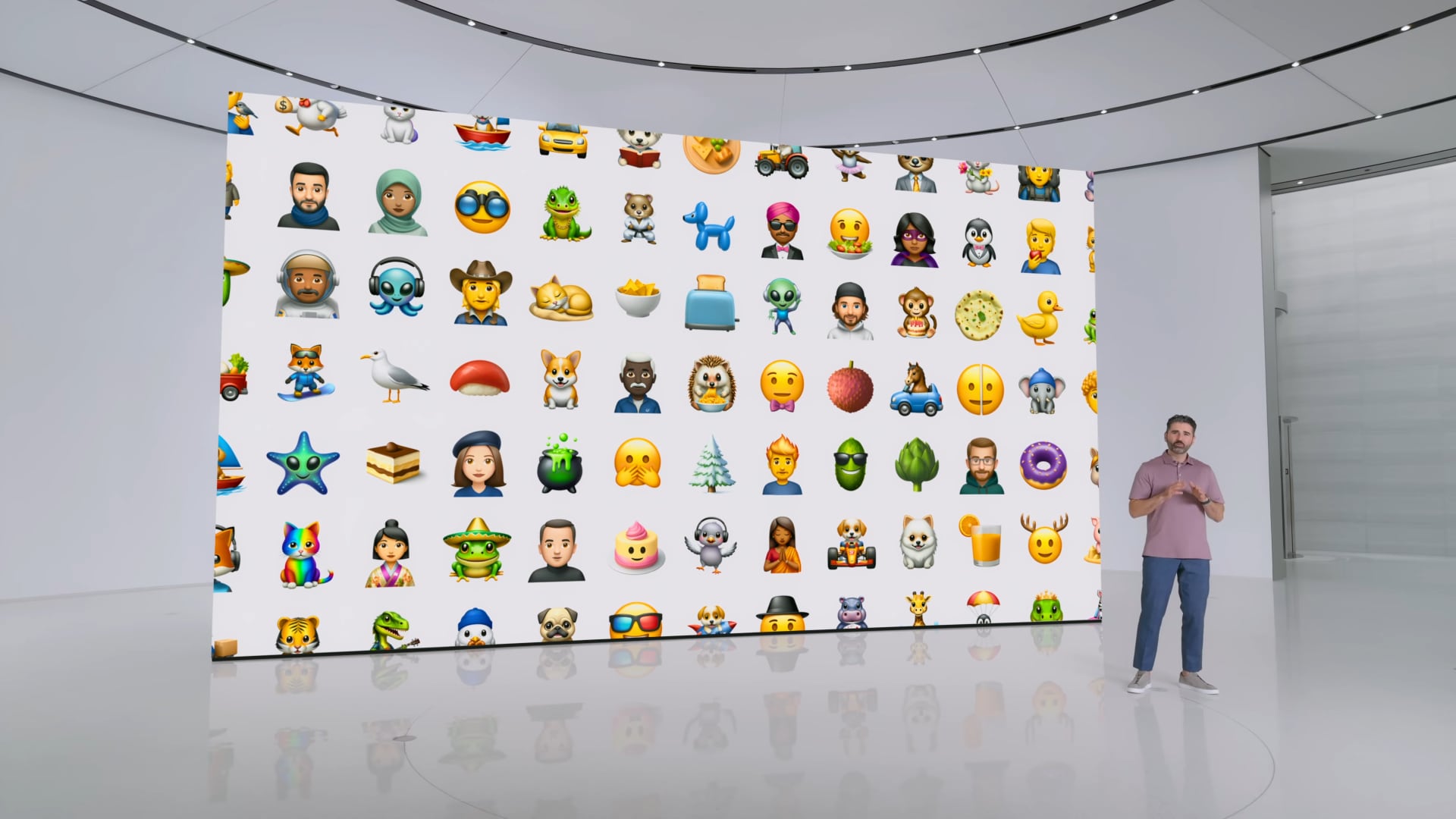 An Apple executive standing in front of a huge screen displaying a bunch of custom emoji characters, called Genmoji.