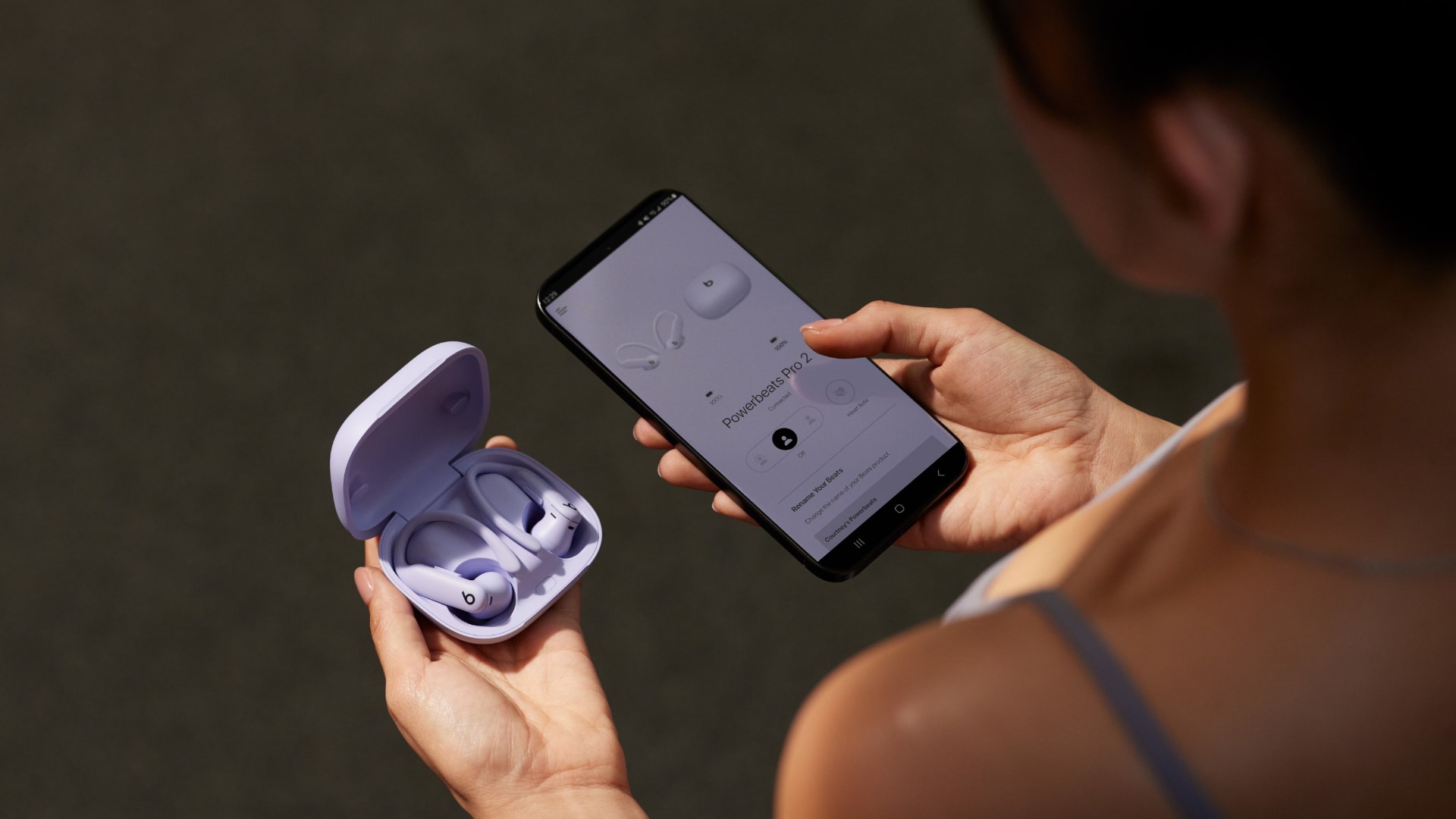 Female athlete holding Powerbeats Pro 2 in their charging case and iPhone showing a card to pair and set up the earphones.