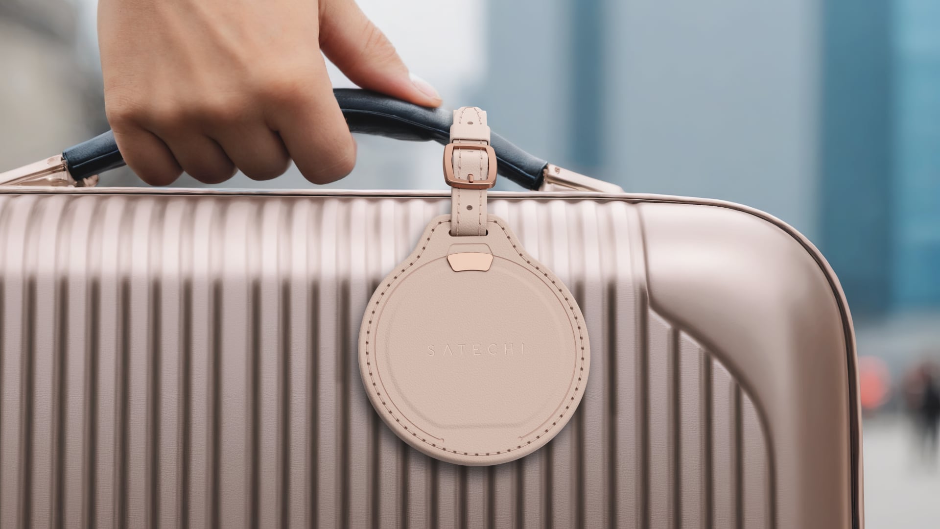 Hand holding luggage with Satechi's luggage tag hanging on the handle.