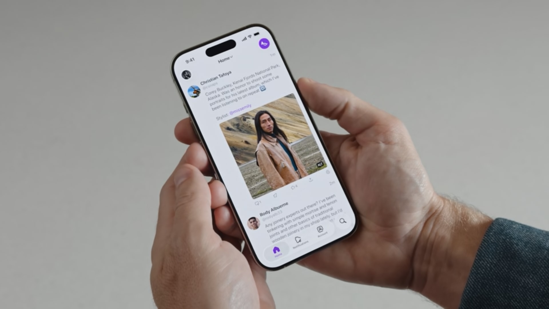 iPhone held in hands, showing a social media app with a post showcasing a young man wearing a stylish jacket.